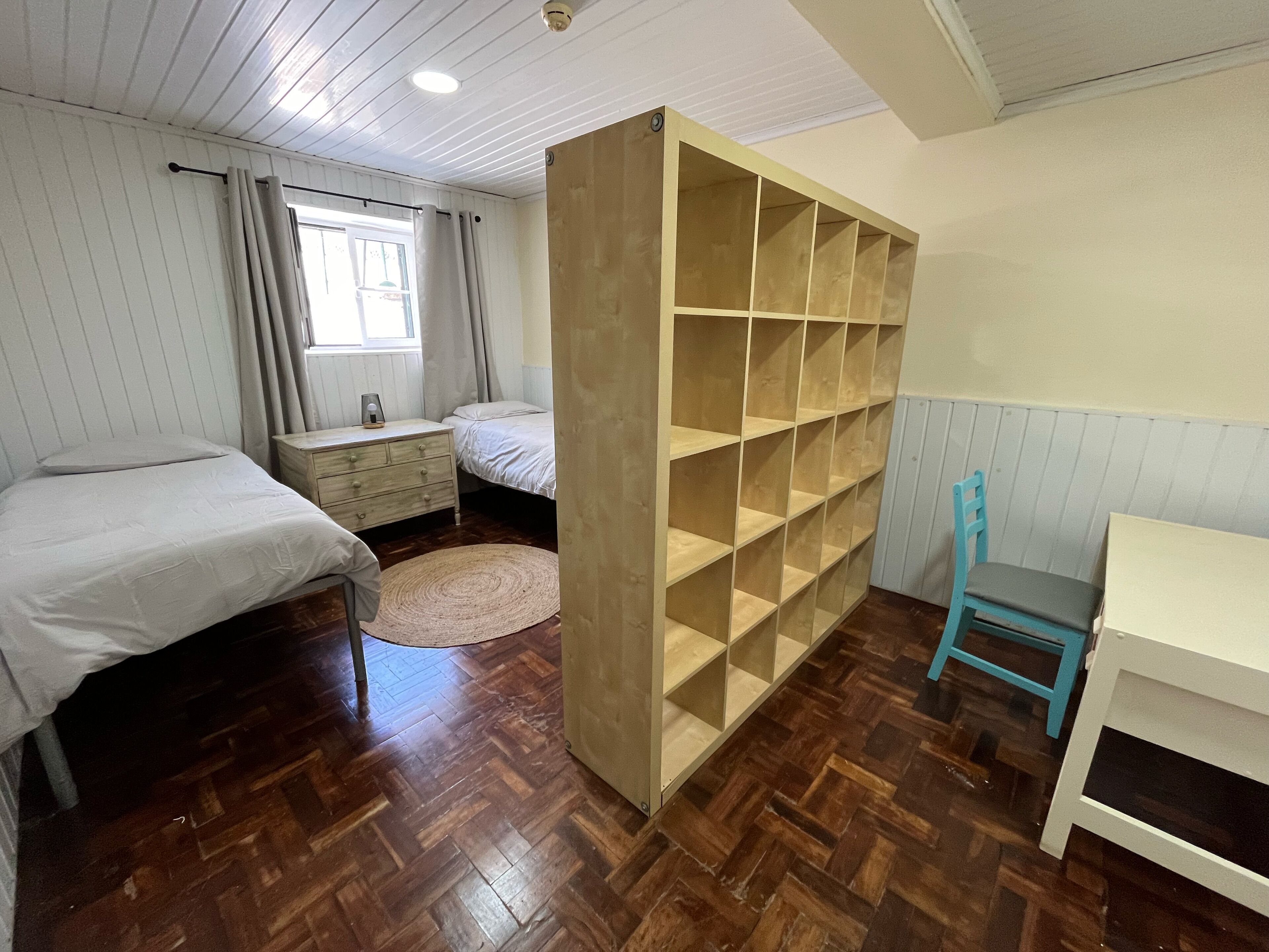 A bedroom with two beds, a wooden wardrobe, a desk, and a chair.