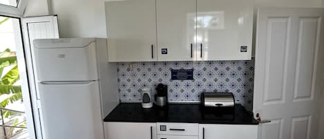 Een kleine keuken met witte kastjes, een zwart aanrecht en een koelkast.