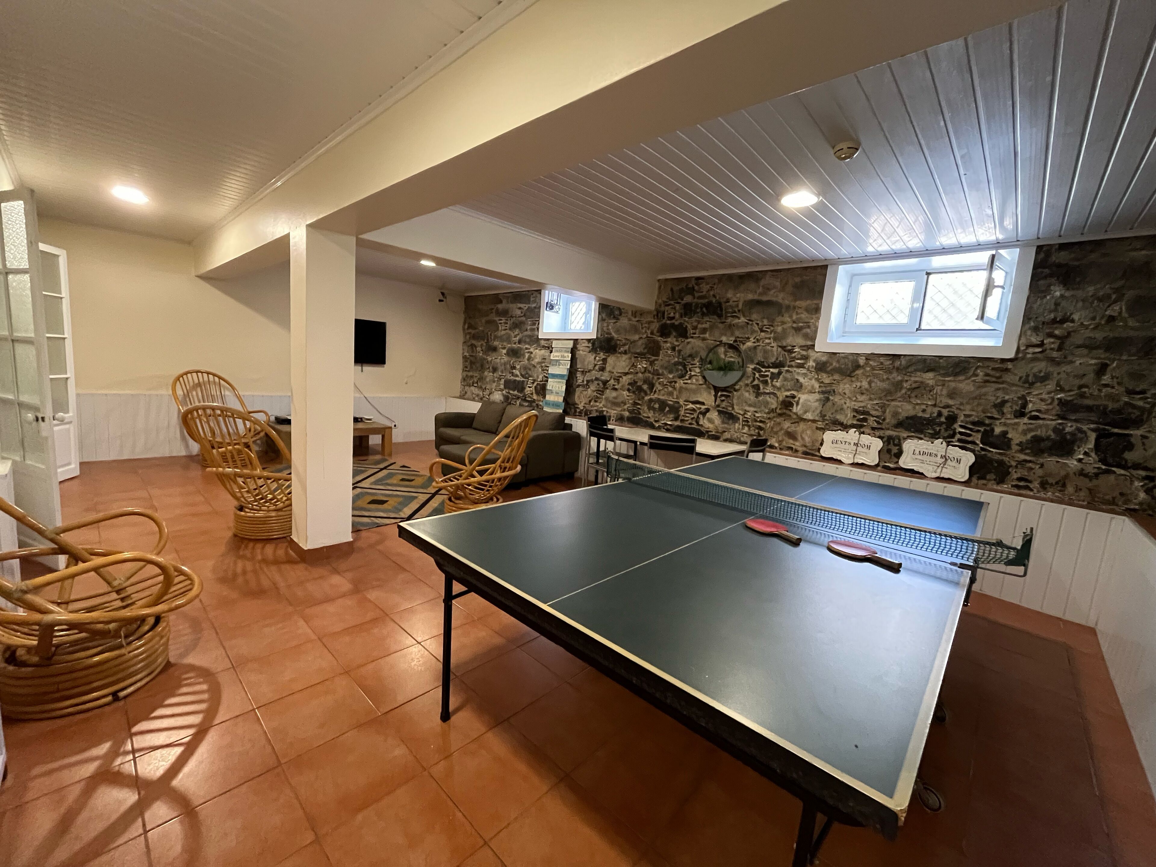 A ping pong table in a room with stone walls, wicker chairs, and a television.