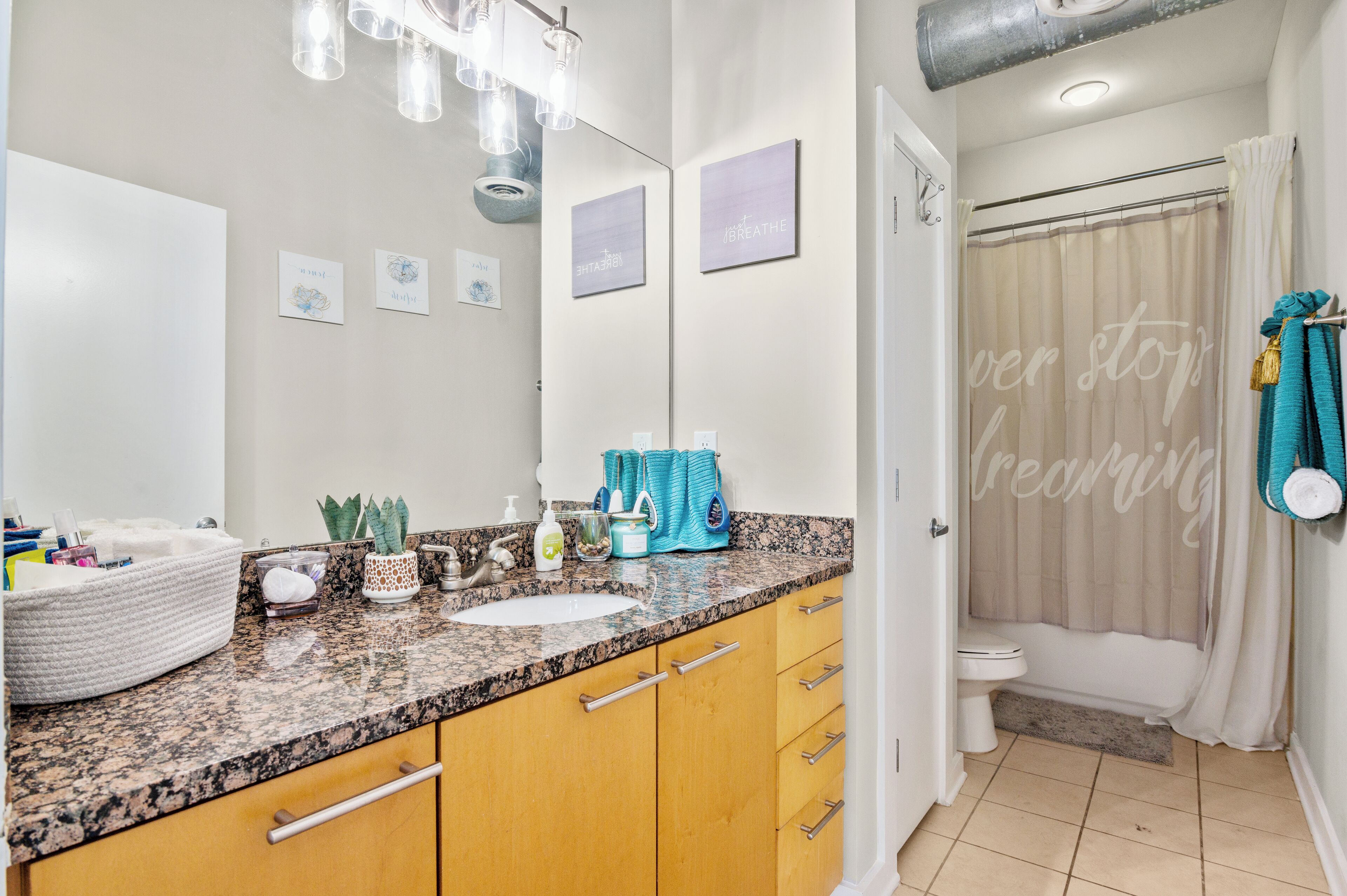 A bathroom with a granite countertop, a white sink, a mirror, and a shower curtain with a motivational phrase.