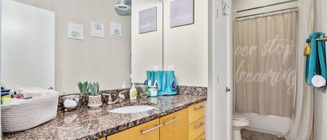 A bathroom with a granite countertop, a white sink, a mirror, and a shower curtain with a motivational phrase.