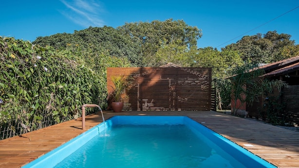 A rectangular swimming pool with a wooden deck surrounding it, a wooden fence, and lush greenery in the background. - Elegant and Complete Chalets in Imbituba - REL (Imbituba)
