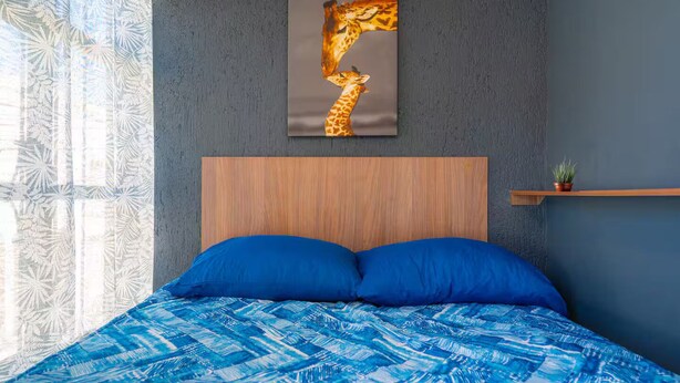 A bedroom with a bed, a headboard, a wall-mounted giraffe painting, and a window with patterned curtains. - Studio in the heart of Morelia! (Morelia)