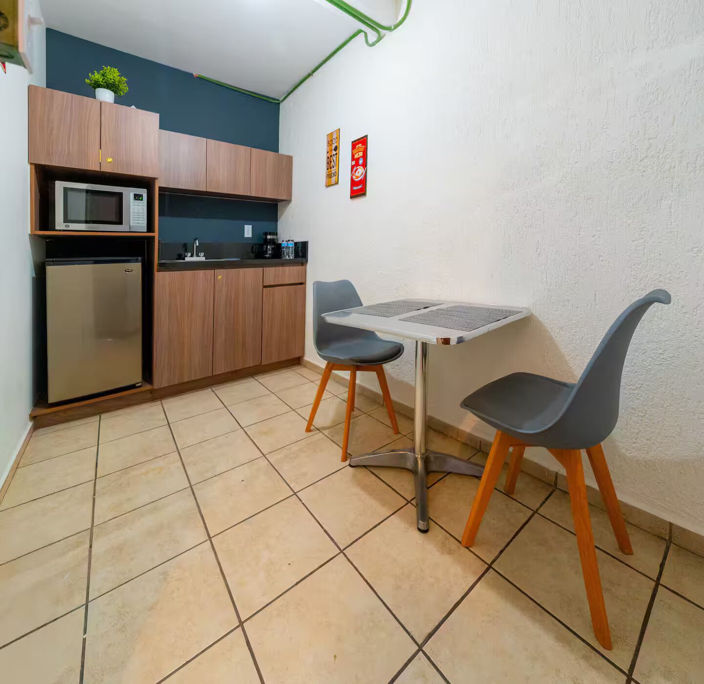 Eine kompakte Küche mit Mikrowelle, Kühlschrank und Holzschränken. Auf der Arbeitsfläche steht ein kleiner Tisch mit zwei Stühlen und ein Blumentopf.