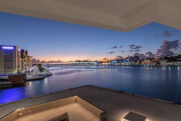A waterfront hotel with a view of the river and city skyline at dusk.