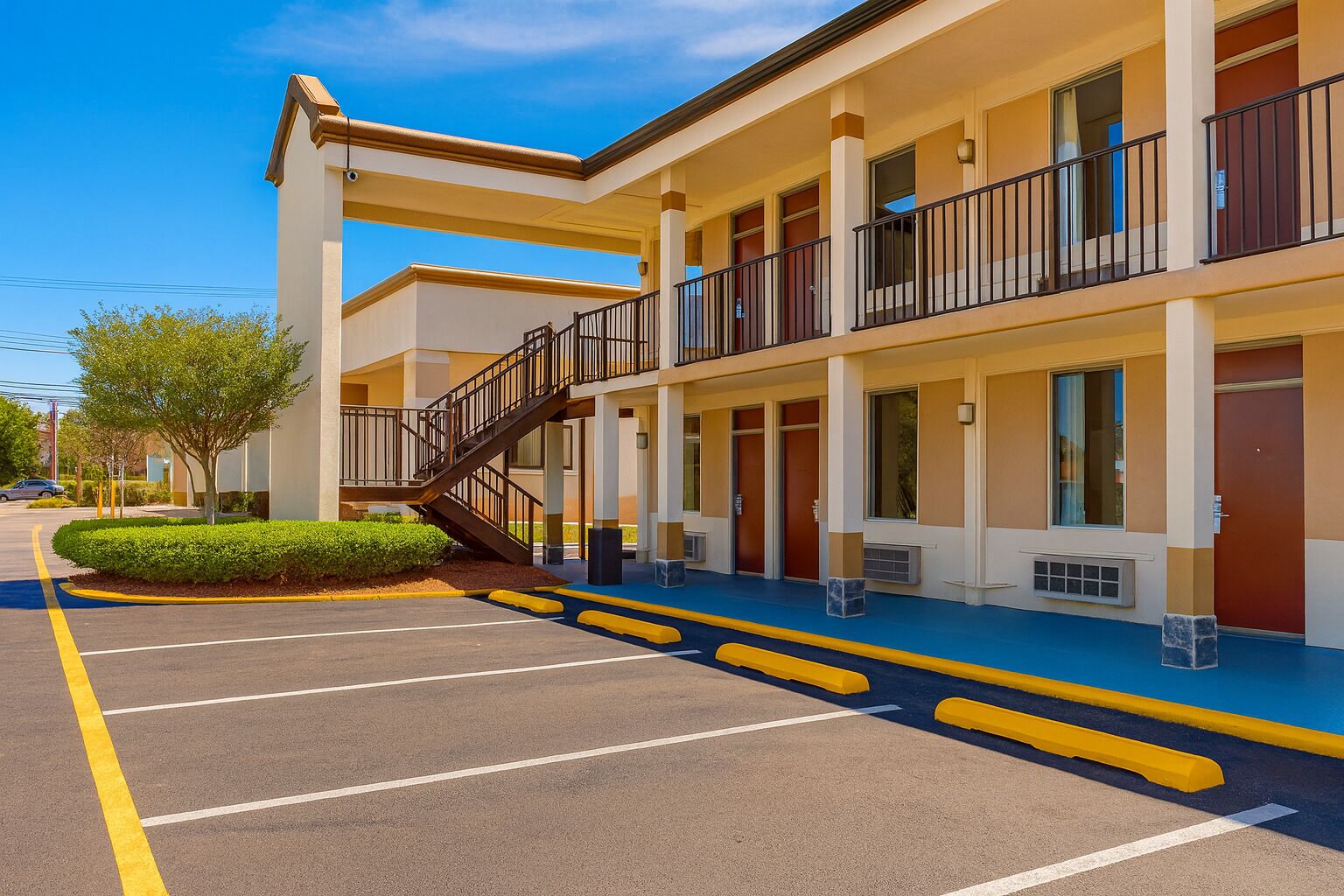 Un motel à plusieurs étages, doté d’un escalier central, d’un parking et offrant une vue sur un ciel dégagé.