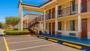 Un motel à plusieurs étages, doté d’un escalier central, d’un parking et offrant une vue sur un ciel dégagé.