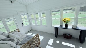 Ein helles Zimmer mit einem Bett, einem Schreibtisch und großen Fenstern mit Blick auf eine grüne Landschaft.