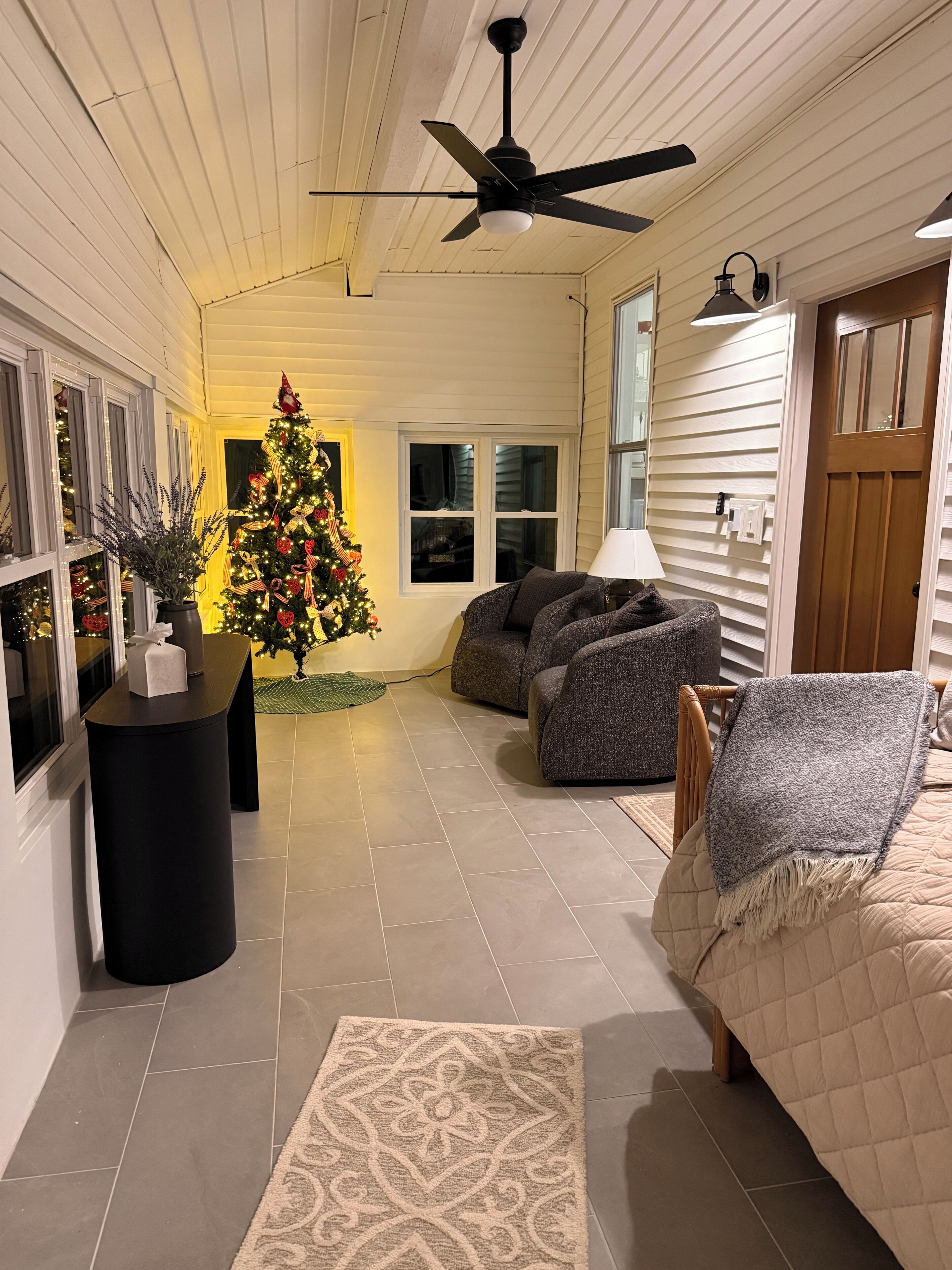 Un salon chaleureux avec un grand sapin de Noël, un ventilateur de plafond et un coin salon confortable.