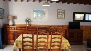 A dining area with wooden chairs and a table, a wooden cabinet with a television, and a map on the wall.