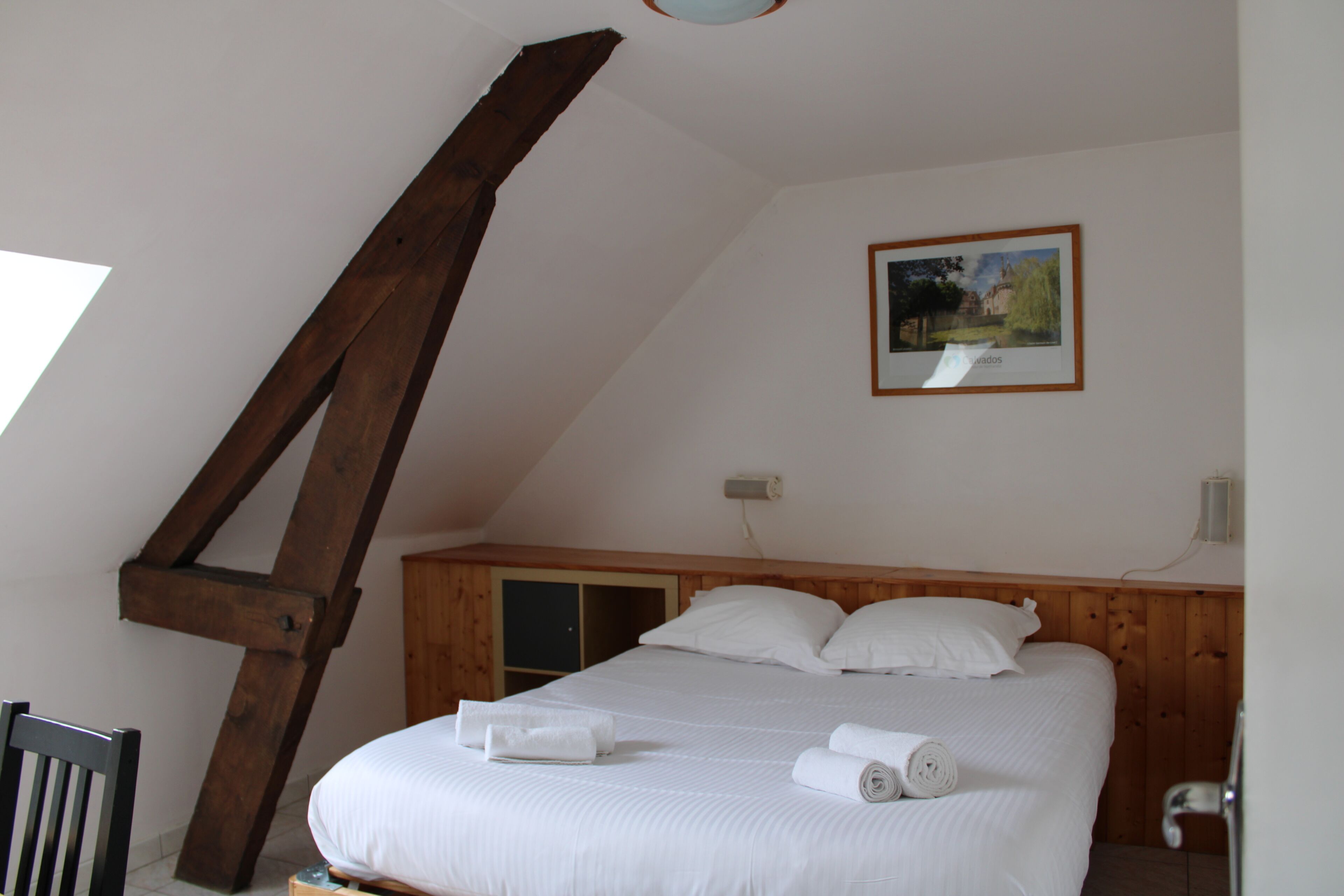 A bedroom with a wooden headboard, a bed with white linens, a painting on the wall, and a wooden ladder.