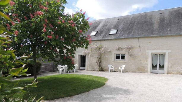 A building with a gravel courtyard, white chairs, and a tree with pink flowers.