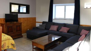 A living room with a dark-colored sofa, a wooden coffee table, a television on a wooden cabinet, and a window with curtains.