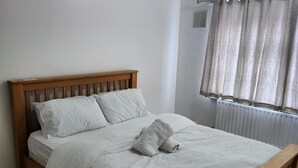 A bed with a wooden headboard, white bedding, and a rolled towel. - Dagenham - House - Stay5 - Parking - Greatlocation (Dagenham)