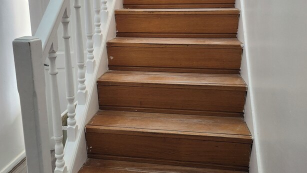 Eine Holztreppe mit weißen Spindeln und einem Holgitter, die zu einer oberen Etage führt.