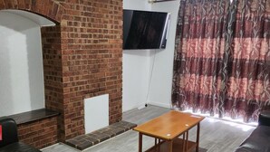 Ein Wohnzimmer mit Kamin aus Ziegelsteinen, einem flachbildschirmfernseher darüber, einem Holztisch und einem schwarzen Ledersofa.