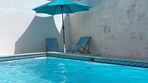 A swimming pool with clear blue water, two lounge chairs, and a blue umbrella. - HOTEL MONTESILVA (Puerto Plata)