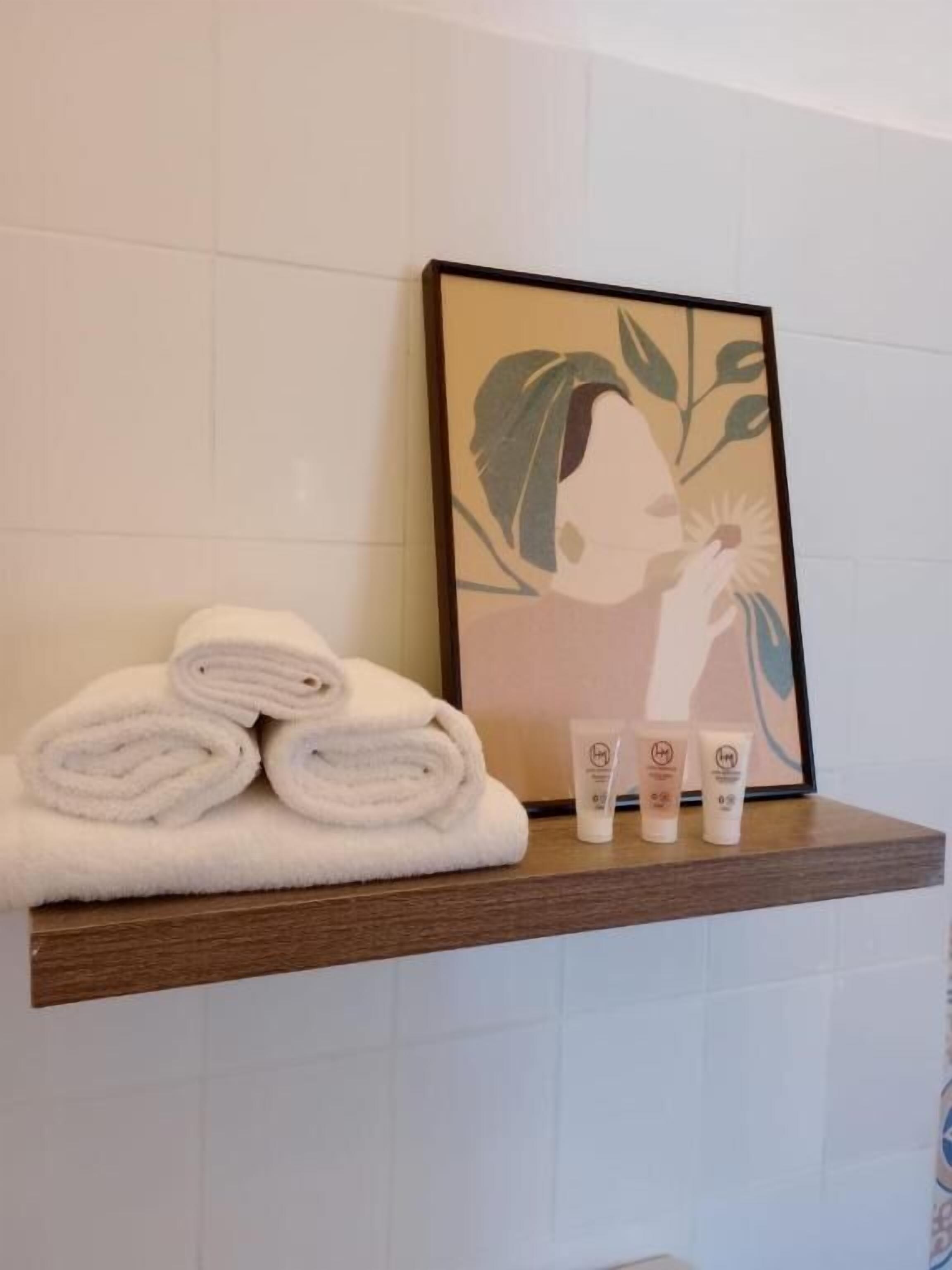 A bathroom with a wooden shelf holding rolled towels and three toiletry bottles.
