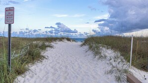 A sandy beach path with a warning sign, grassy dunes, and a cloudy sky. - Luxury Waterfront Villa w/ Pool, Hot Tub, Dock & Game Room - Sleeps 28 (Pensacola)