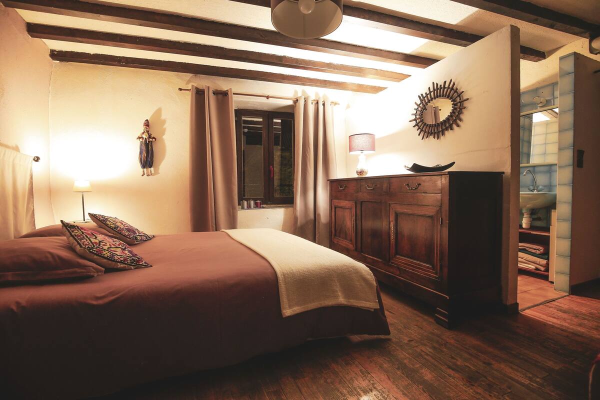 A bedroom with a bed, wooden dresser, and a mirror on the wall.