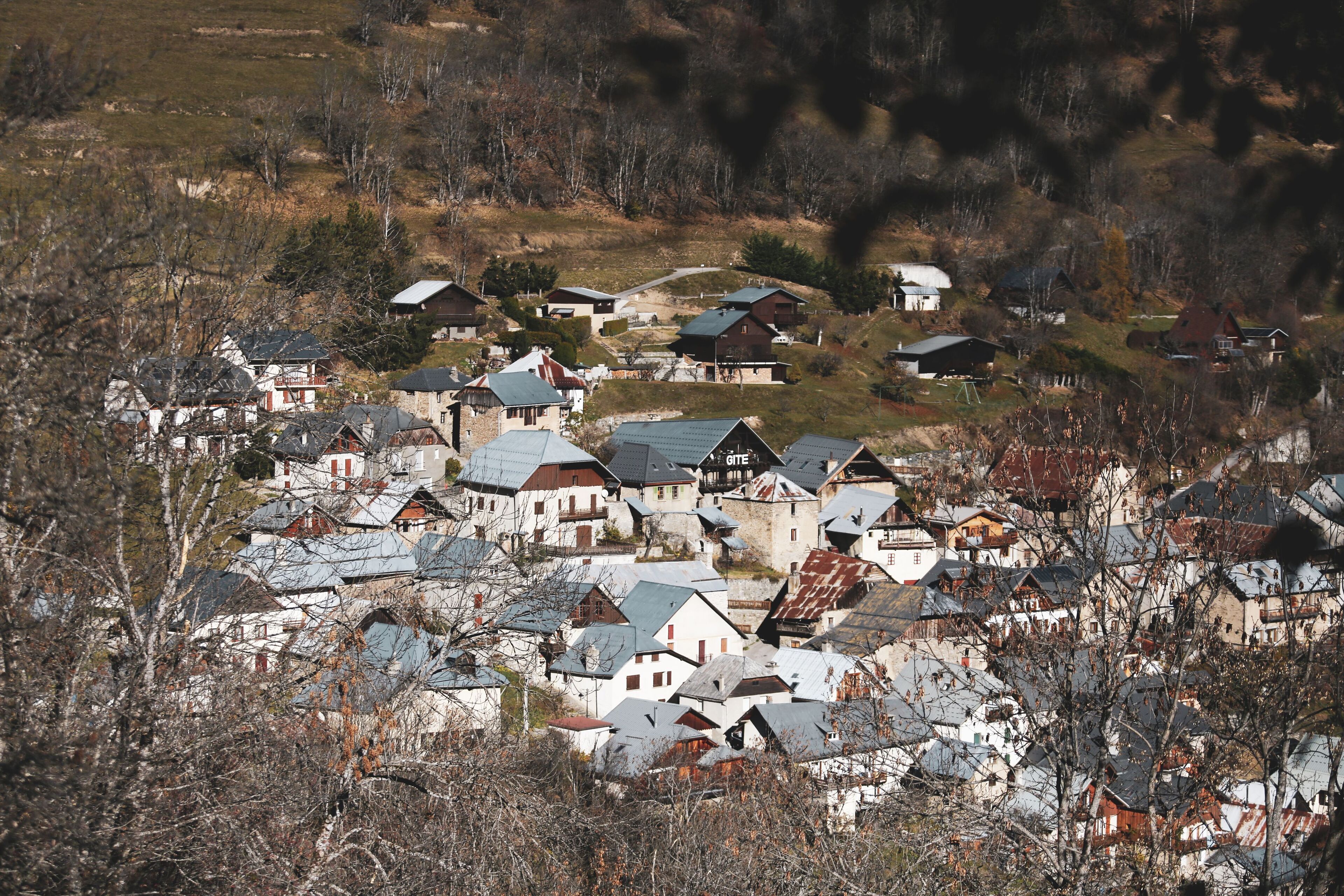 A cluster of traditional houses with steep roofs, surrounded by trees and hills.