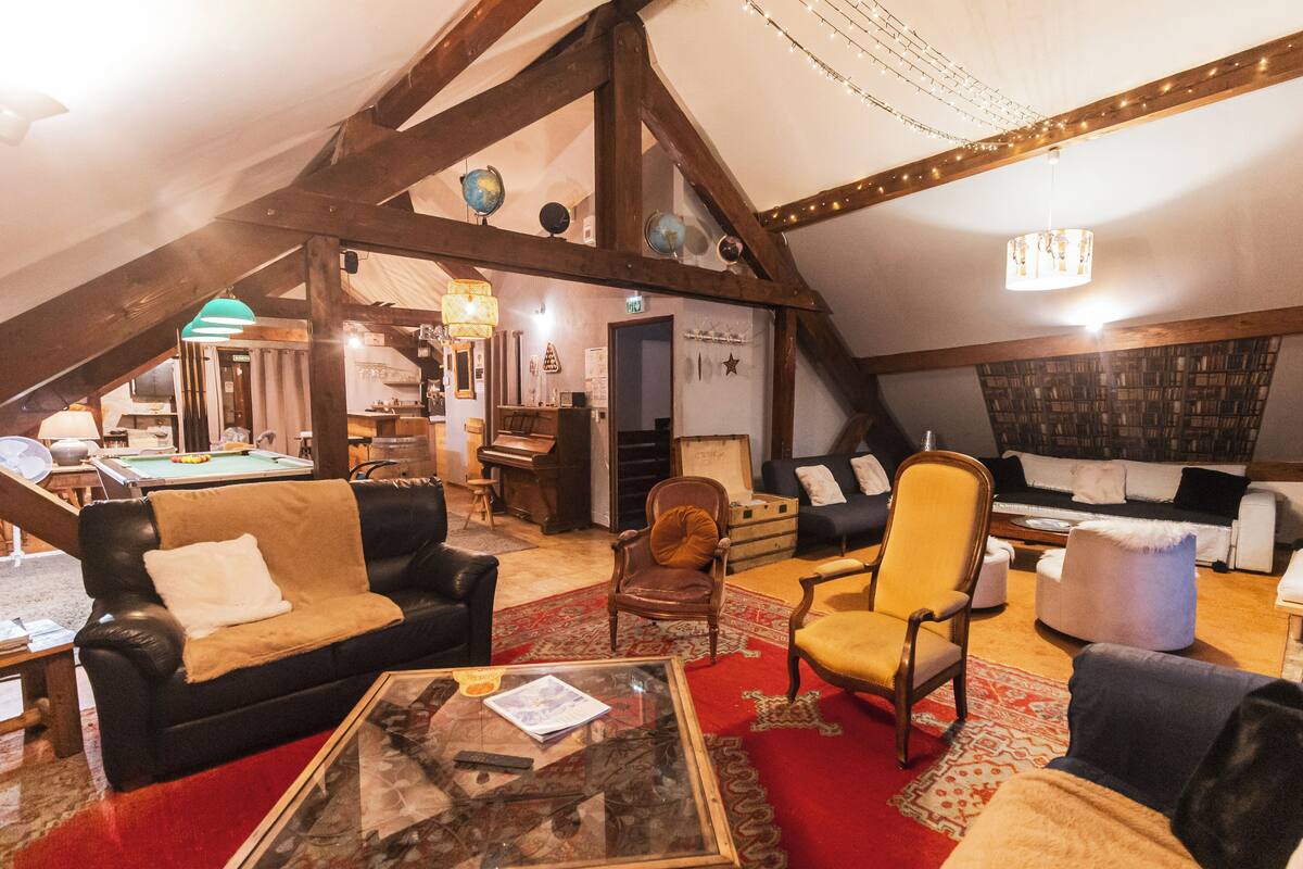 A cozy attic room with a loft bed, a billiards table, and a variety of seating options including a sofa, armchairs, and a small table.