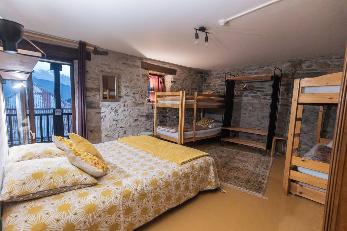 A bedroom with a bed, bunk beds, a window with a view, and a stone wall.