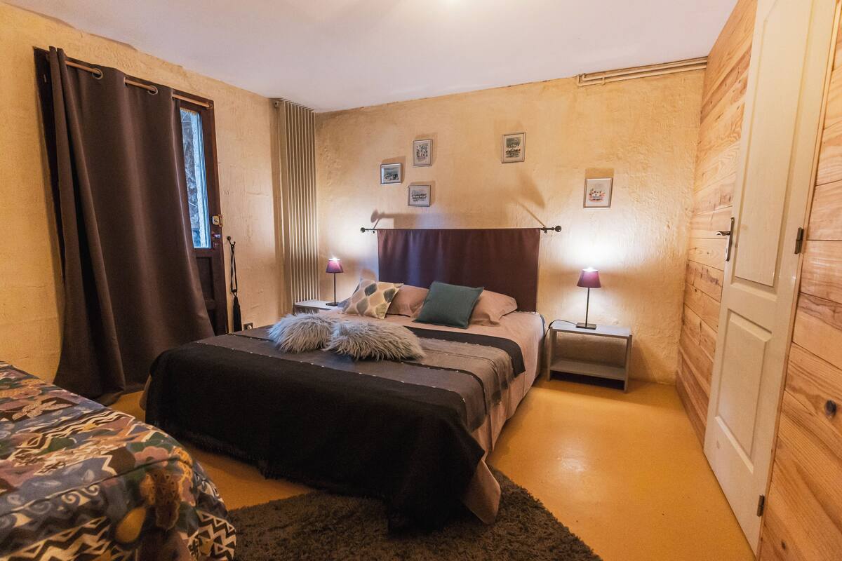 A bedroom with a bed, bedside tables, a window with curtains, and a wooden door.