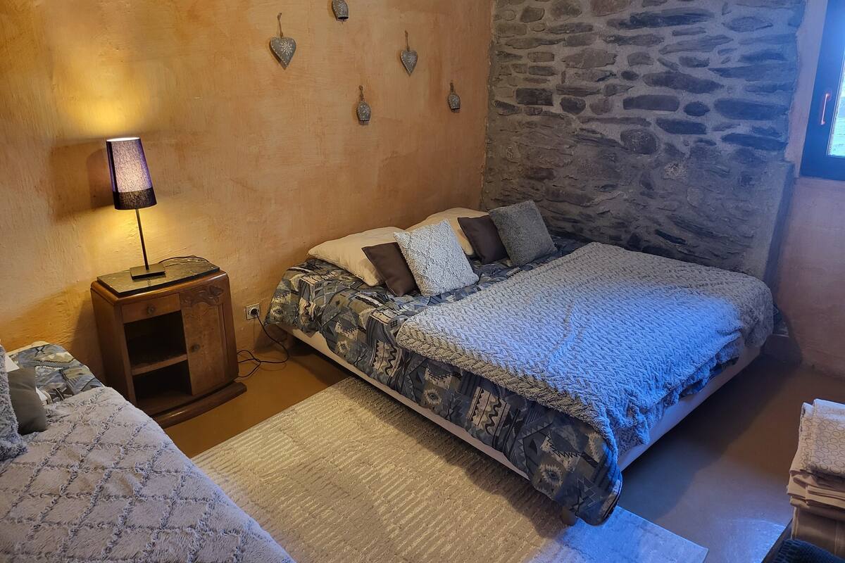 A cozy bedroom with a bed, a nightstand, a lamp, and a stone wall.