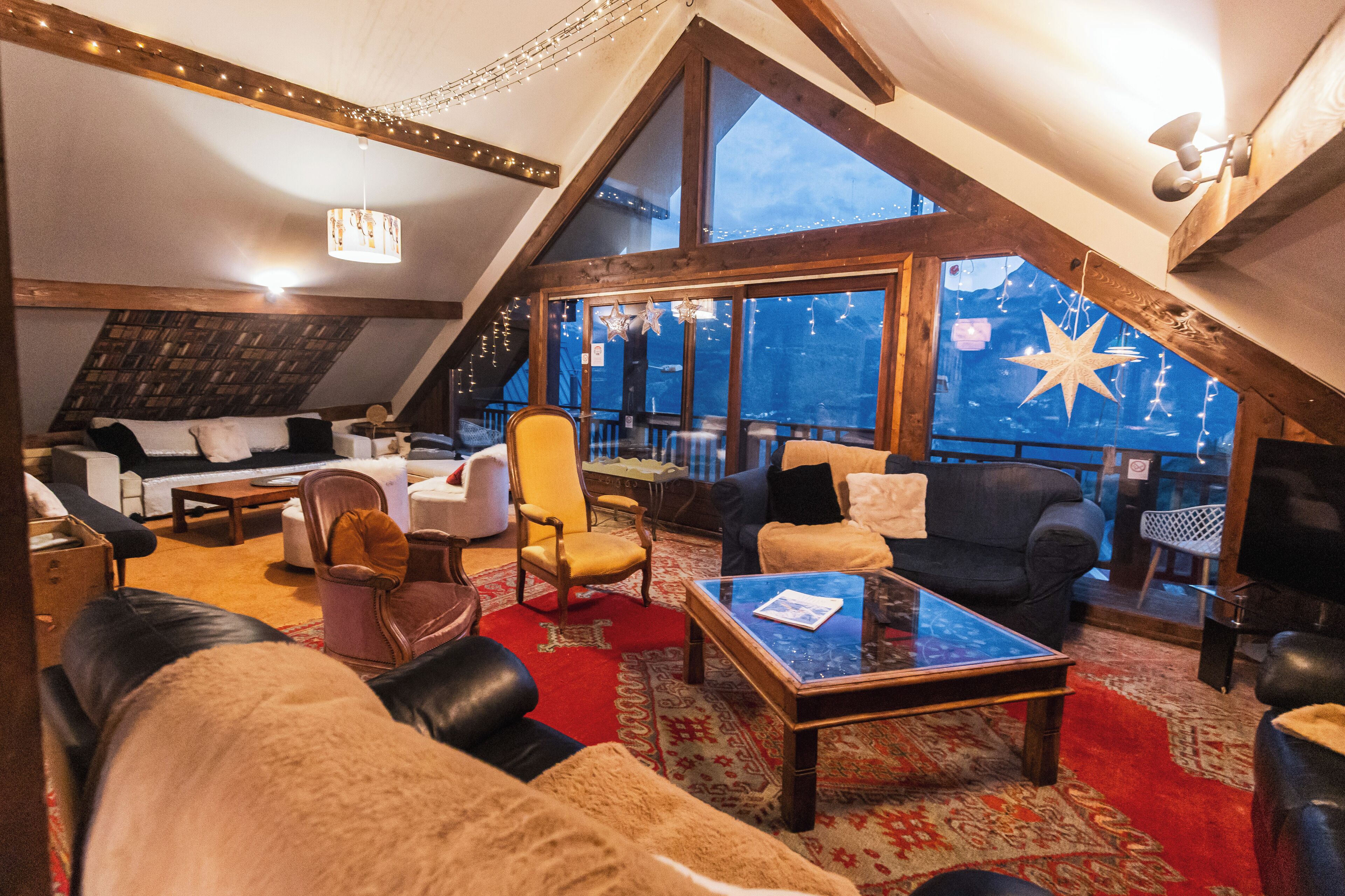 A cozy, well-lit loft-style room with a large window, comfortable seating, and a red carpet.