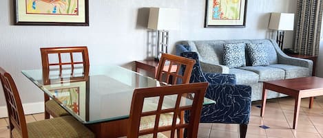 Un coin repas comprenant une table en verre, des chaises en bois, un canapé et deux lampes fixées au mur.