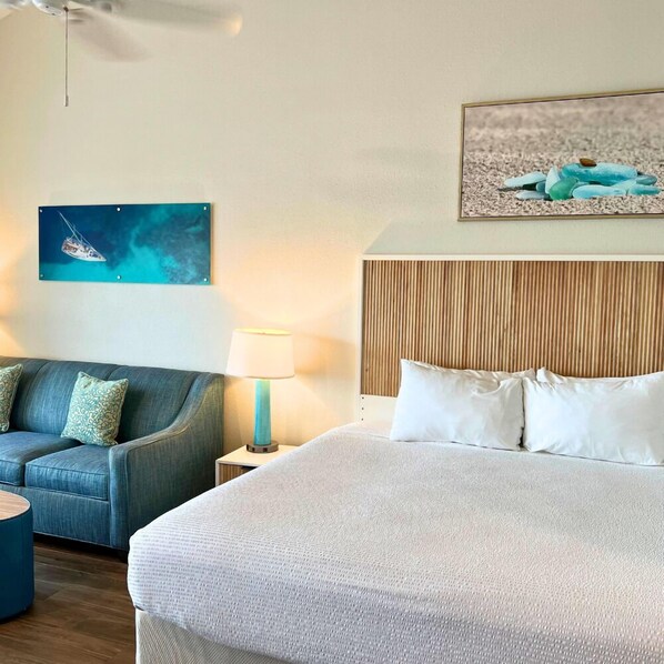 Une chambre d’hôtel avec un grand lit, un canapé, une table de chevet avec une lampe et un mur orné d’un tableau représentant un voilier.