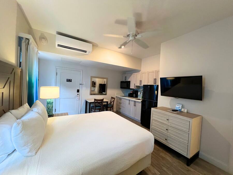 A hotel room with a bed, a desk, a chair, a TV, a ceiling fan, and a kitchenette.