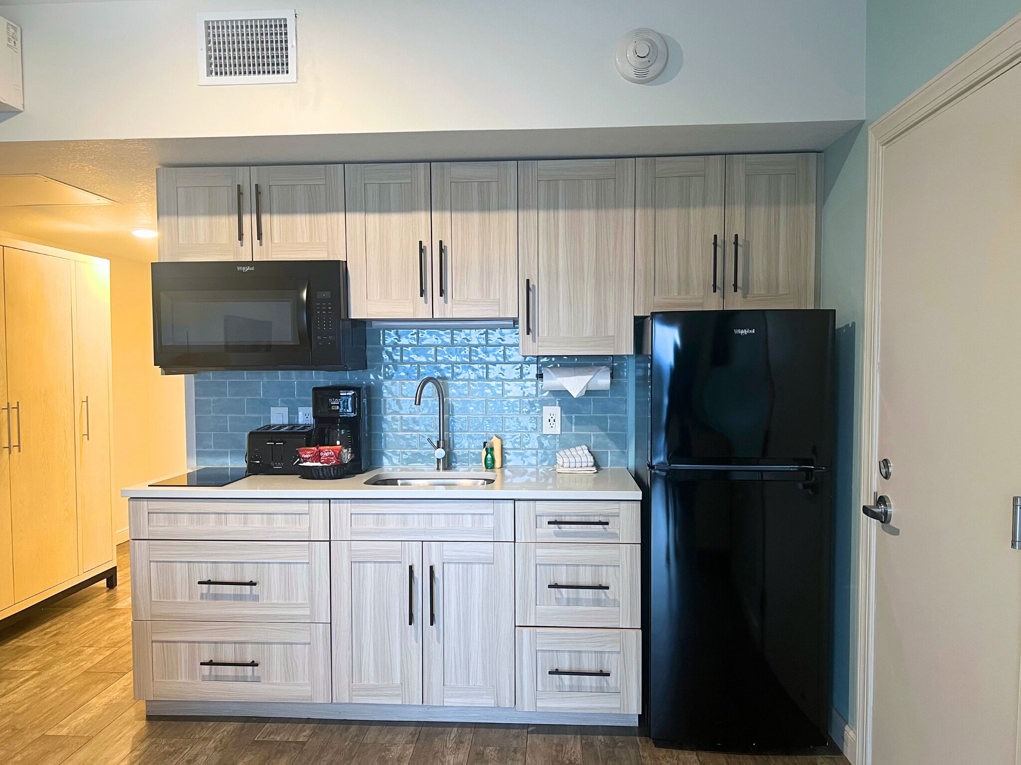 Una cocina moderna con armarios de madera clara, un refrigerador negro, un microondas y una cafetera.