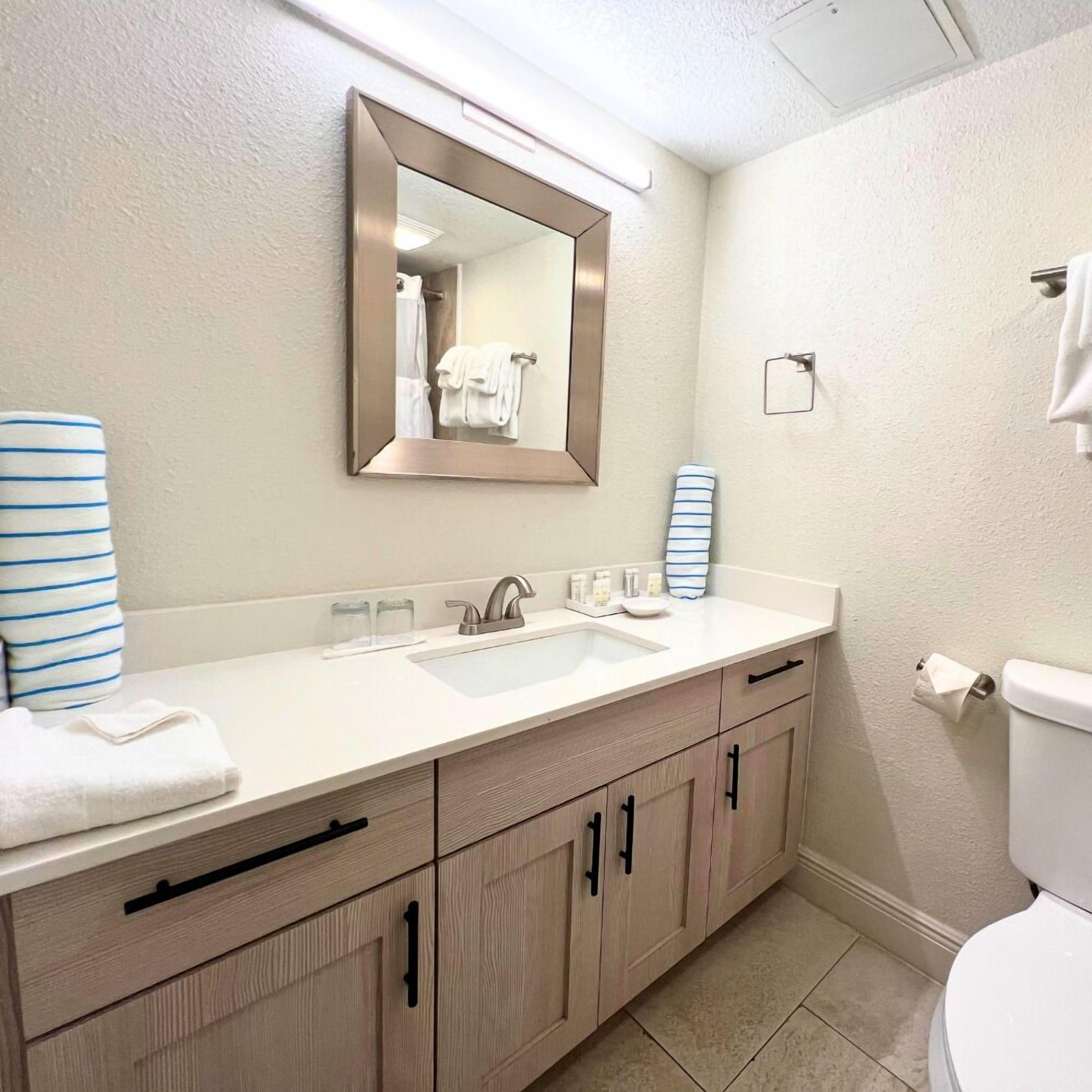 Un baño con lavamanos blanco, espejo y armarios de madera.