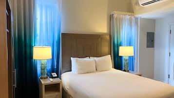 Habitación de hotel con una cama, dos mesitas de noche con lámparas, un teléfono y una ventana con cortinas.