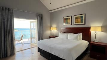 A hotel room with a large bed, two bedside lamps, a ceiling fan, and a balcony with a view of the sea.