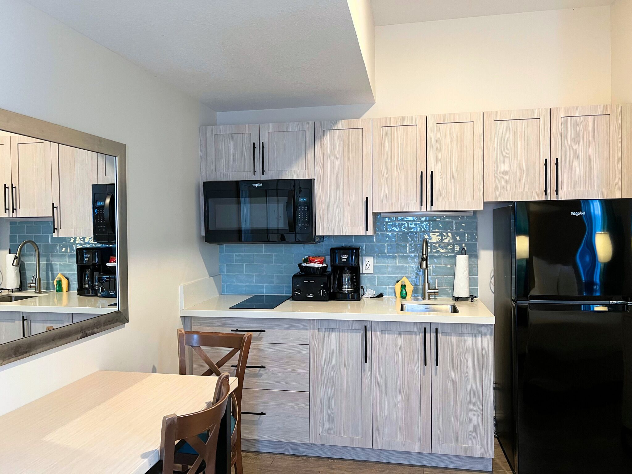 Een moderne keuken met lichte houten kastjes, een zwarte koelkast, een magnetron en een koffiezetapparaat.