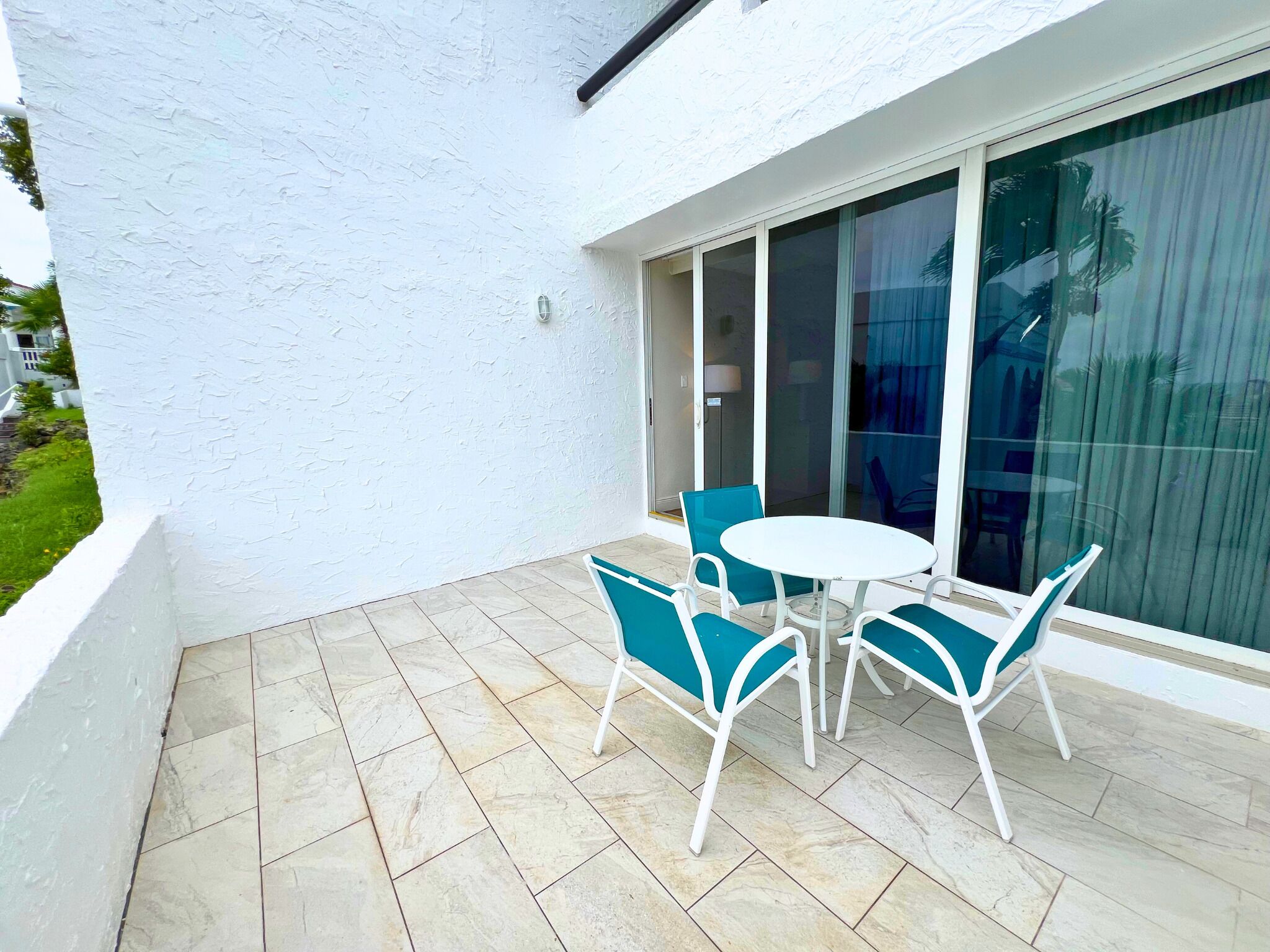A patio with a white table and blue chairs, a tiled floor, and a white wall.