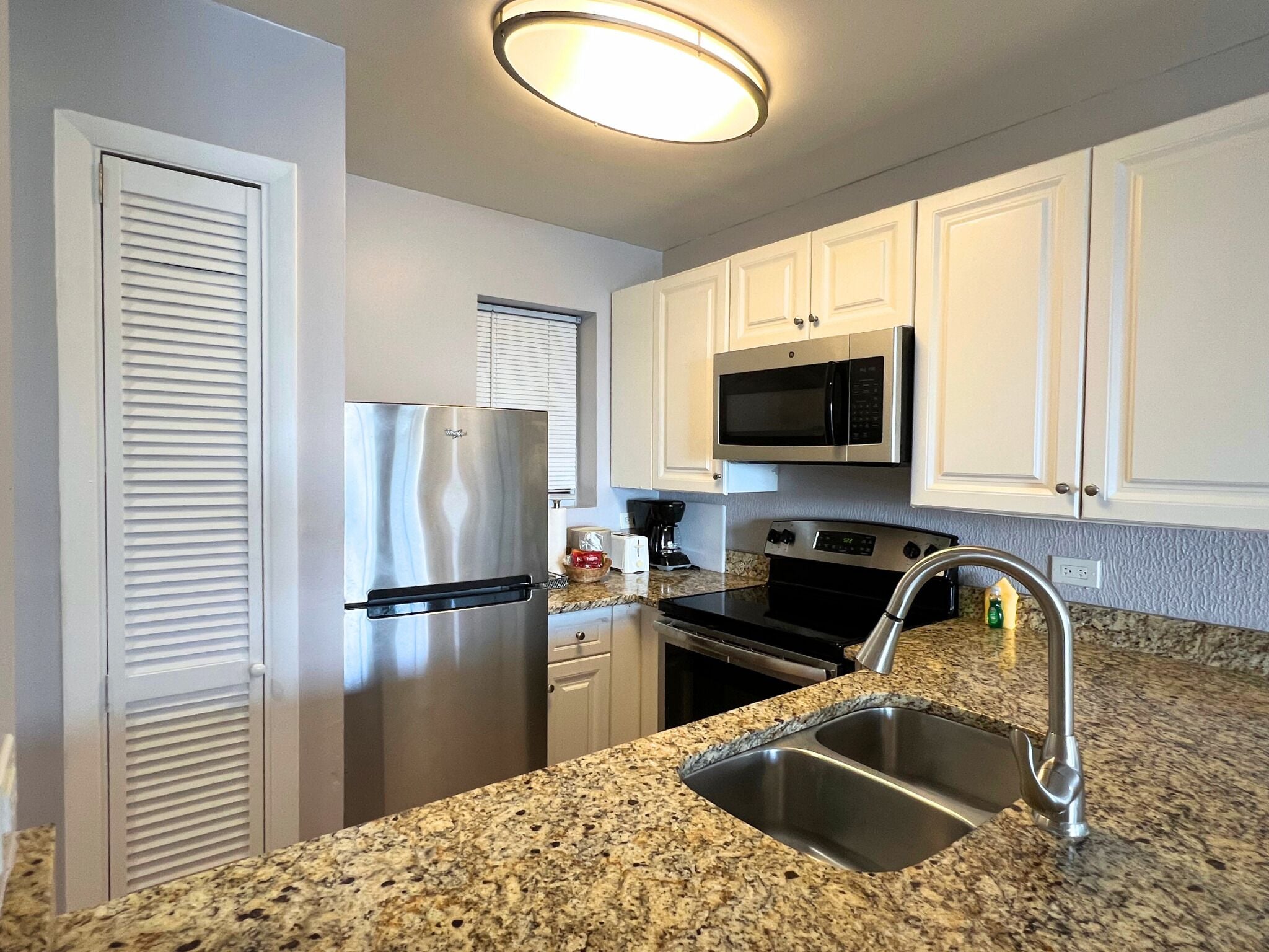 A kitchen with white cabinets, stainless steel appliances, granite countertops, and a stainless steel sink.