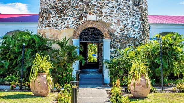 A stone building with a staircase leading to an entrance, surrounded by potted plants and a clear sky. - Bluebeard's Castle Resort (Charlotte Amalie)