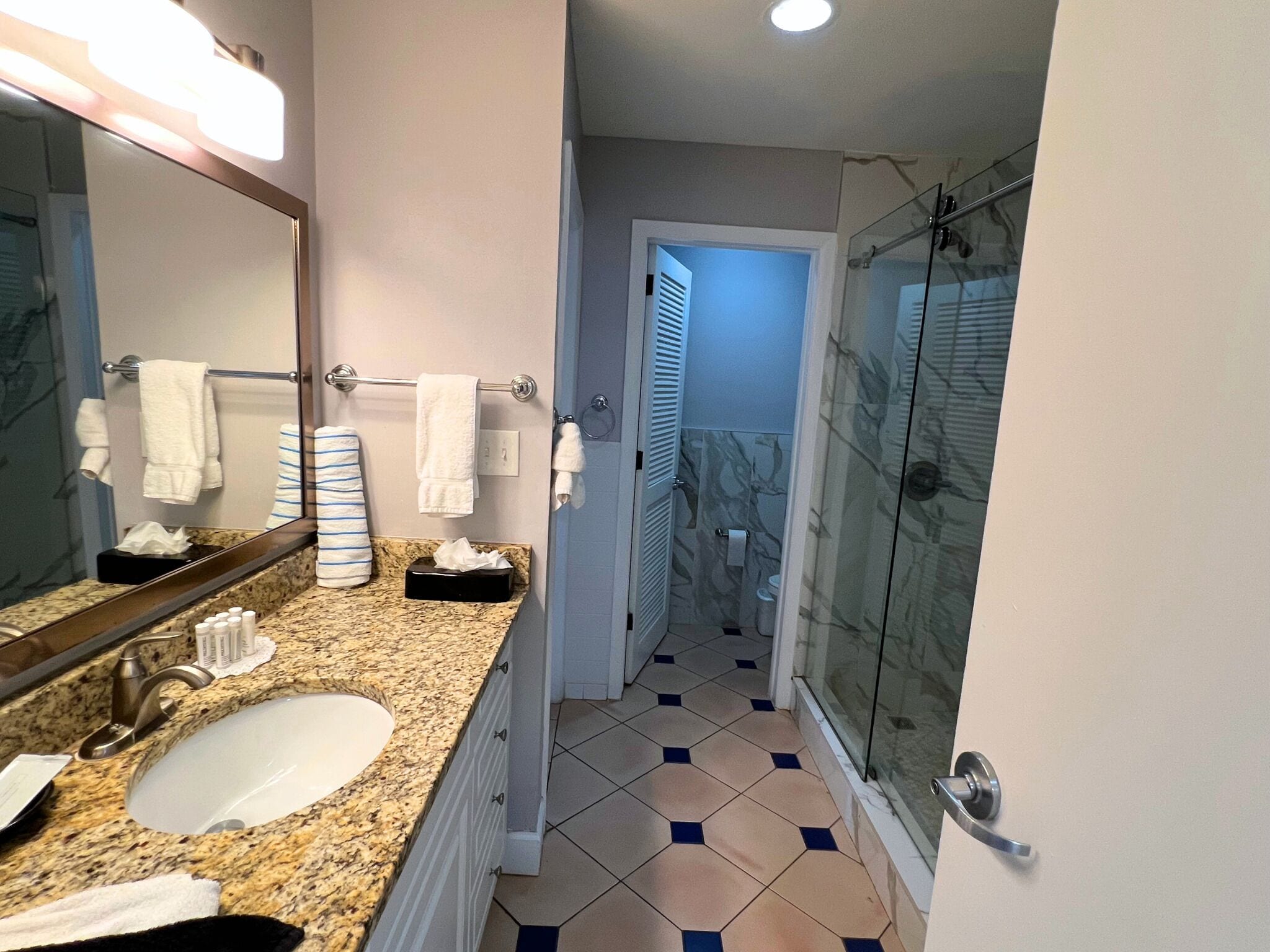 A bathroom with a granite countertop, a white sink, a glass shower enclosure, and a mirror with a towel rack.