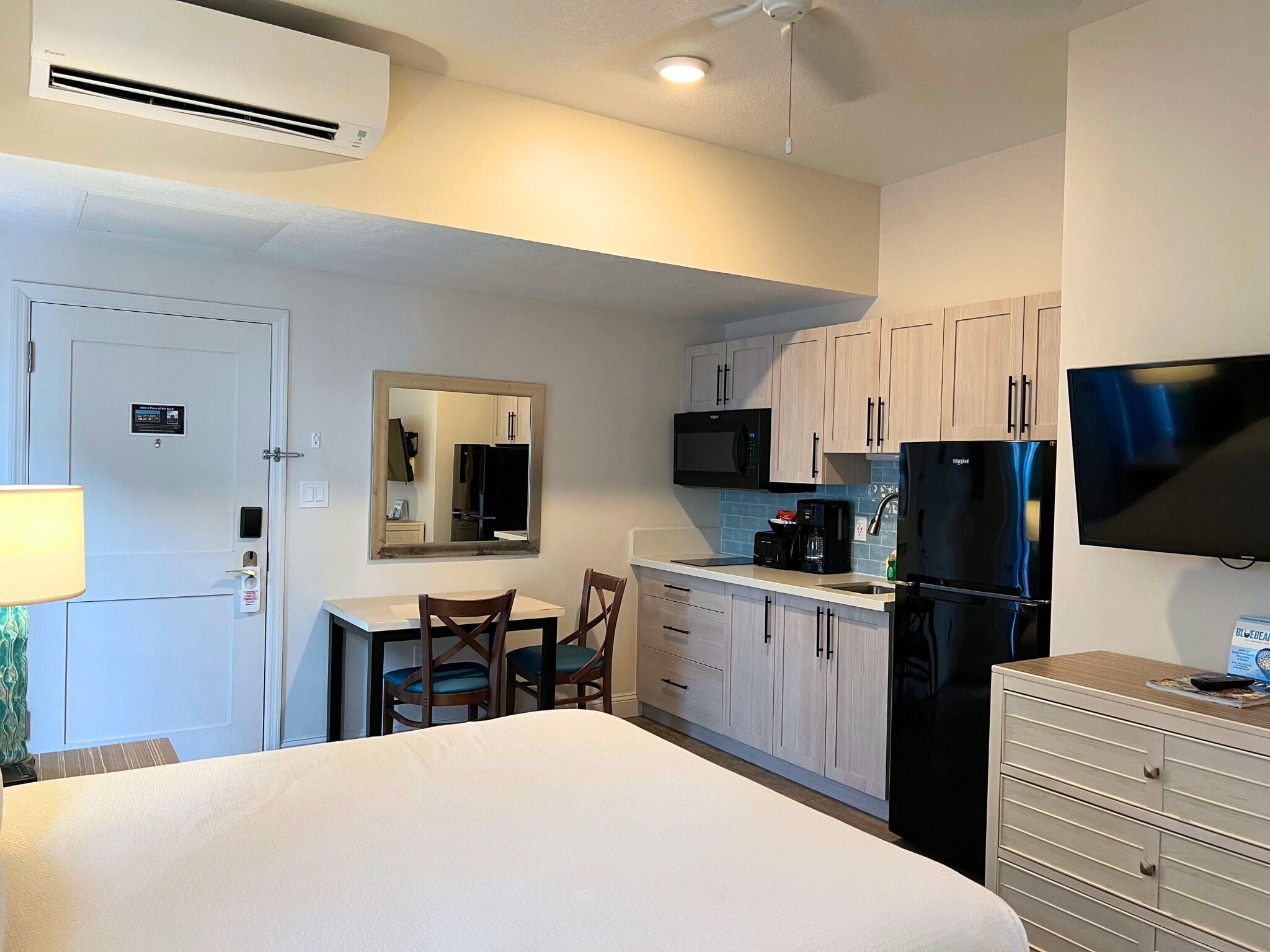 A hotel room with a bed, a desk, a chair, a microwave, a refrigerator, a television, and a mirror.