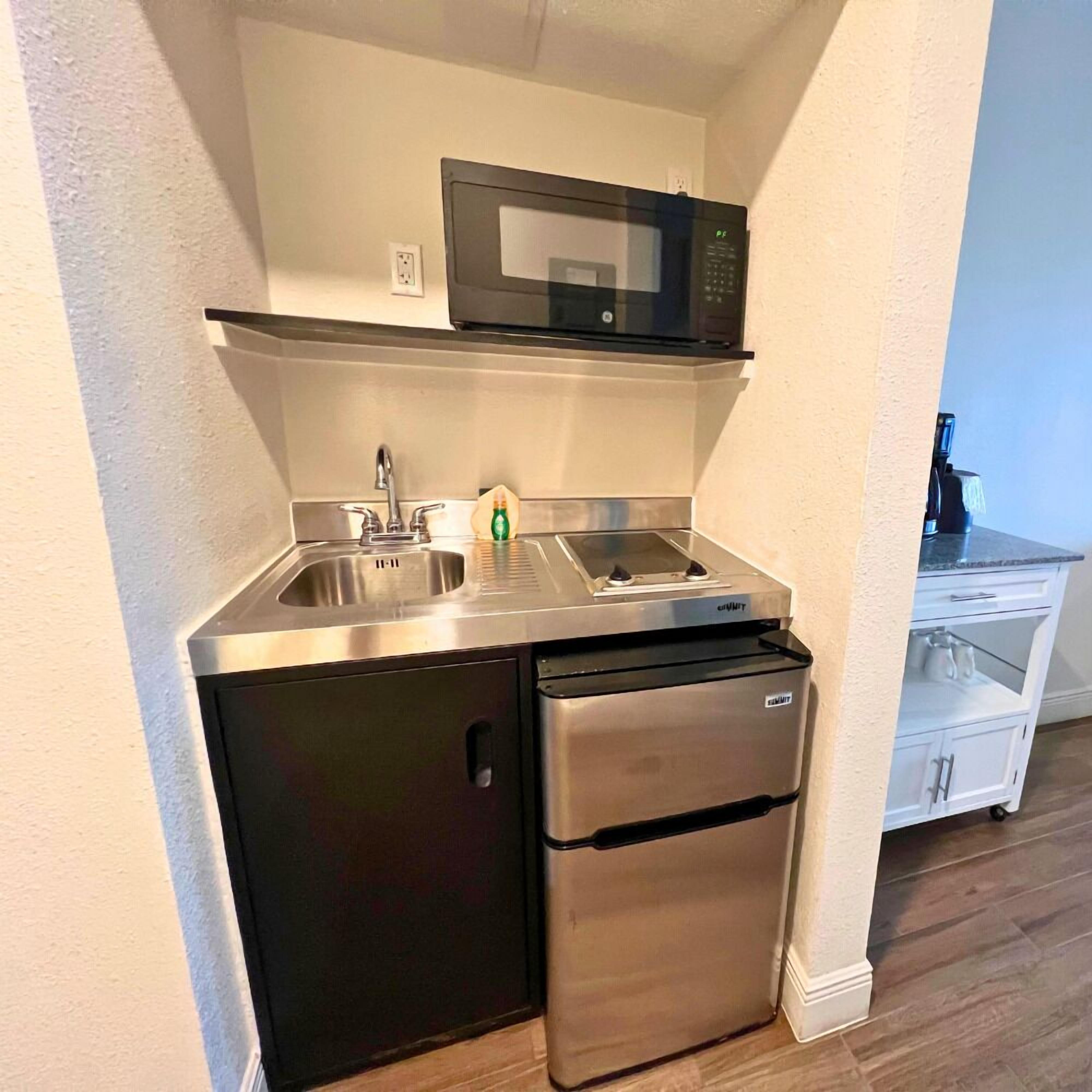 A compact kitchen with a stainless steel refrigerator, a microwave, and a sink.