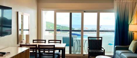 A hotel room with a balcony, a dining area, a sofa, and a TV.