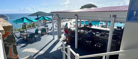 A sunlit outdoor seating area with umbrellas, a pool, and a view of the sea.