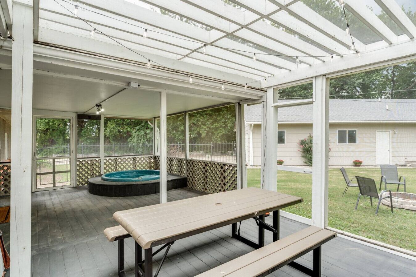 Une terrasse couverte avec un jacuzzi, une table et des chaises.