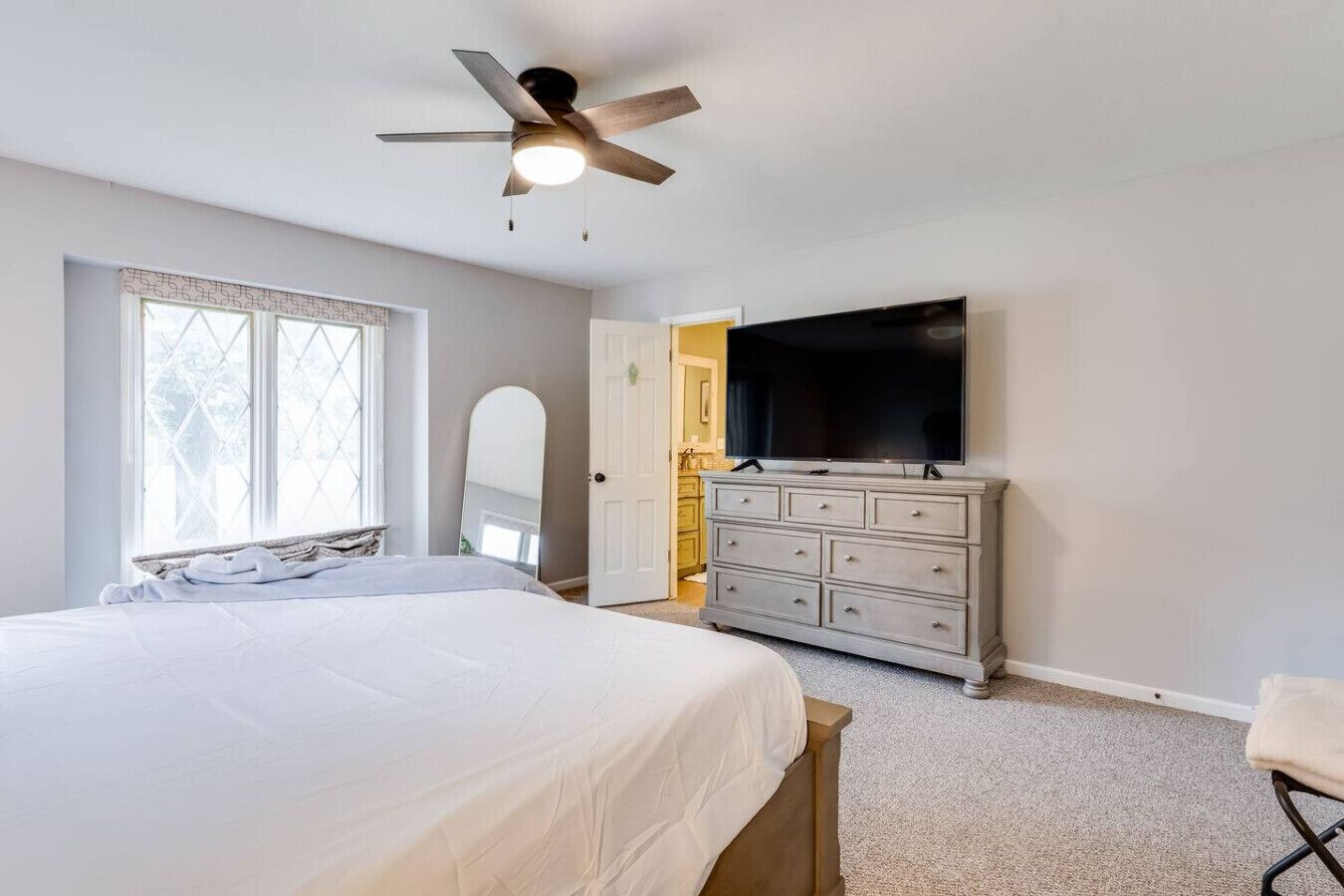 Un dormitorio con cama, cómoda, televisor y ventilador de techo.