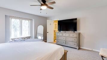 Un dormitorio con cama, cómoda, televisor y ventilador de techo.