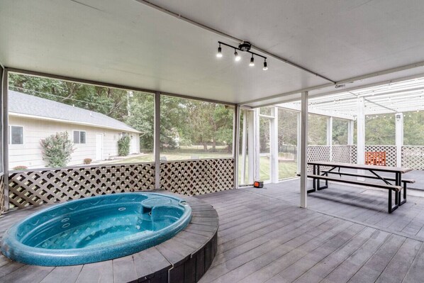 Ein überdachter Außenbereich mit Whirlpool, Holzterrasse und einer Bank.